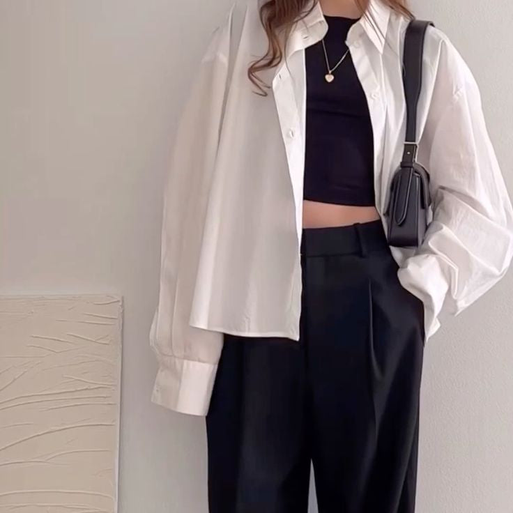 Person wearing a white shirt, black top, and black wide-leg pants with a white background